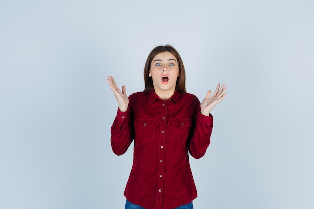 Portrait of girl showing surrender gesture in burgundy shirt and looking shocked