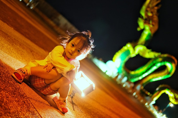 Portrait of girl sitting on illuminated road