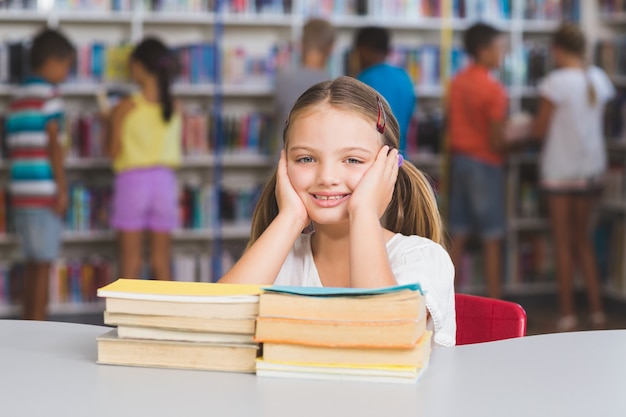 Ritratto della ragazza che si siede con la pila di libri in biblioteca