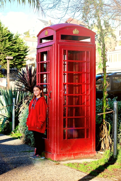 Photo portrait of girl standing against telephone booth