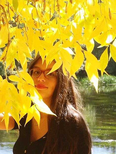 Portrait of girl standing by autumn leaves against lake