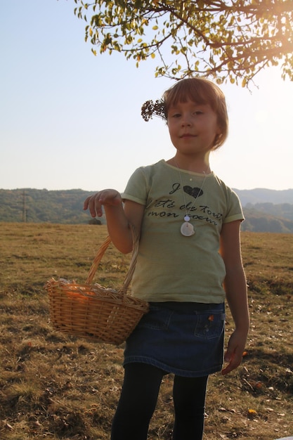 Foto ritratto di una ragazza in piedi accanto al cesto sul campo