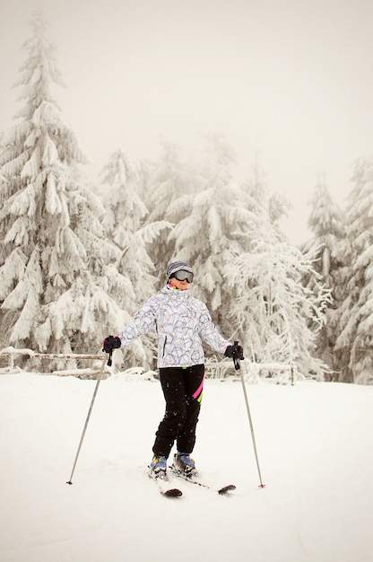 Portrait of a girl standing on skis and posing against snowy mountains and forests