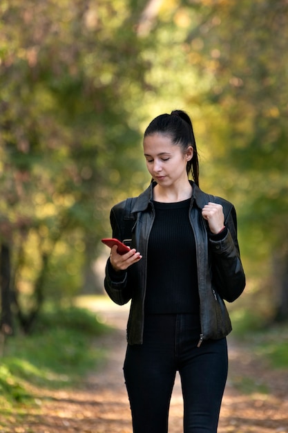 秋の公園で彼女の手で電話を持つ女子学生の肖像画