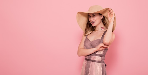 Portrait of a girl in a summer hat and dress on a pink wall