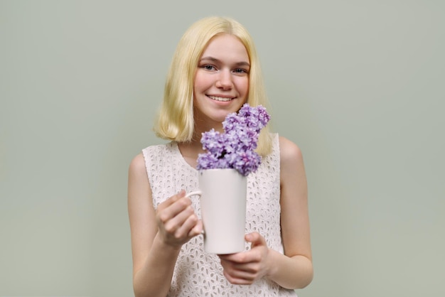 Portrait of girl teenager with flowers on green background. Beautiful female blonde holding lilac in cup. Youth, spring, beauty, cosmetology, health concept