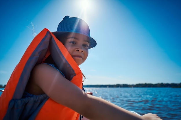 Foto ritratto di una ragazza che indossa un giubbotto di salvataggio mentre è seduta in barca contro il cielo in una giornata di sole