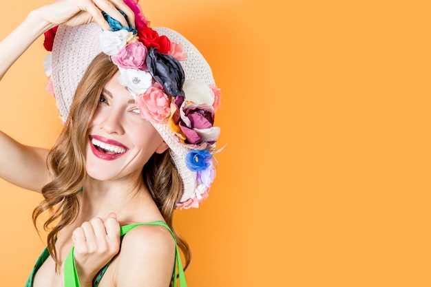 Portrait of a girl wearing summer flower hat over orange bright wall