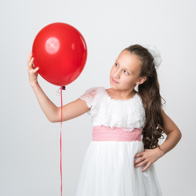 Portrait of girl in white dress holding one red balloon in hand and looking at balloon Studio shot