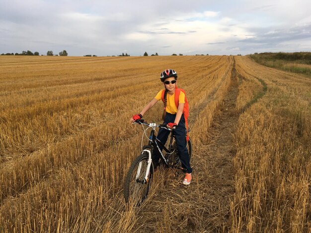 Portrait of girl with bicycle on field against sky