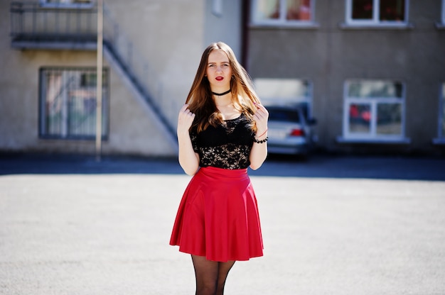 Photo portrait of girl with black choker necklace on her neck and red leather skirt at street of city.