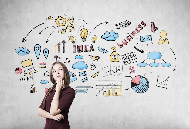 Photo portrait of a girl with braided hair wearing a dark red dress and standing near a concrete wall with colorful business idea icons.