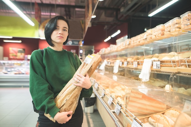Портрет девушки с багетом хлеба в руках супермаркета. красивая девушка позирует в хлебном отделе супермаркета.