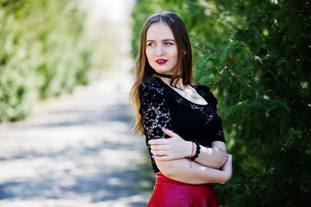 Photo portrait of girl with bright make up with red lips, black choker necklace on her neck and red leather skirt.