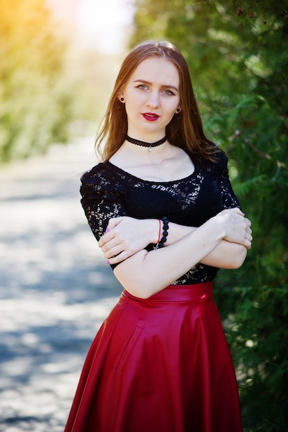 Ritratto di ragazza con trucco luminoso con labbra rosse, collana girocollo nera sul collo e gonna di pelle rossa.