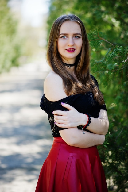 Foto ritratto di ragazza con trucco luminoso con labbra rosse, collana girocollo nera sul collo e gonna di pelle rossa.