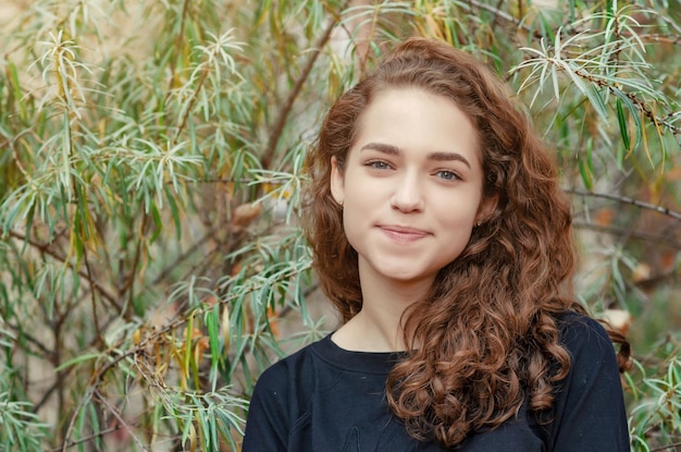 Portrait of a girl with brown curly hair on a background of green bush