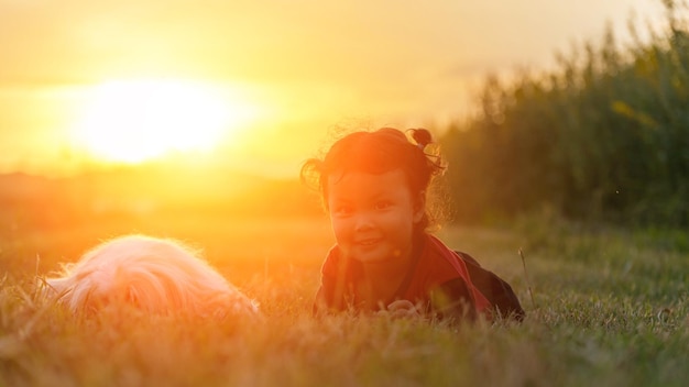 Foto ritratto di una ragazza con un cane sdraiato su un terreno erboso al tramonto