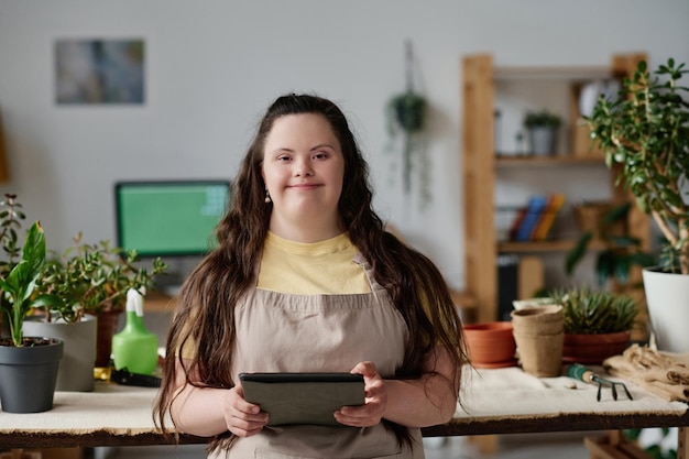 식물을 심는 동안 태블릿 PC를 사용하는 동안 카메라를 보고 웃는 다운증후군 소녀의 초상화