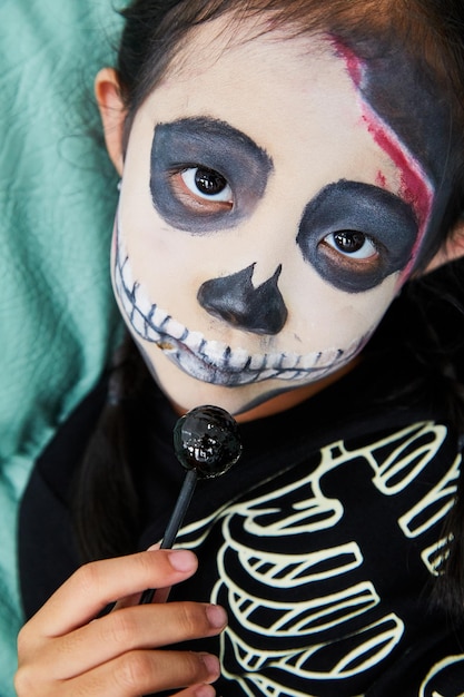 Foto ritratto di una ragazza con la faccia dipinta che tiene un lecca-lecca durante halloween