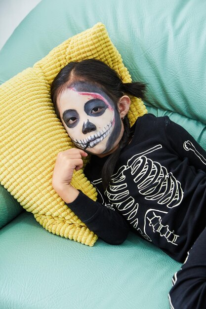 Photo portrait of girl with face paint lying on sofa during halloween