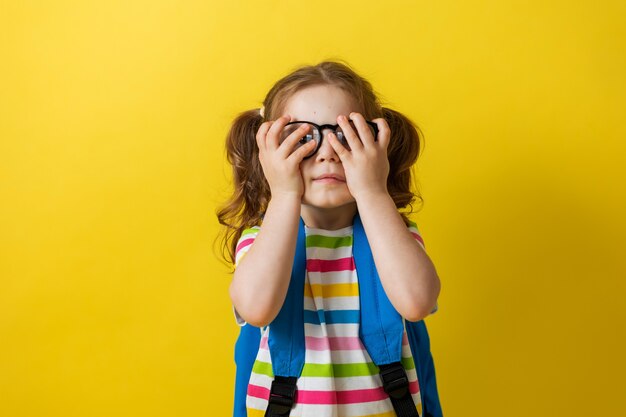 Portrait of a girl with glasses and a striped Tshirt with a school backpack on a yellow background