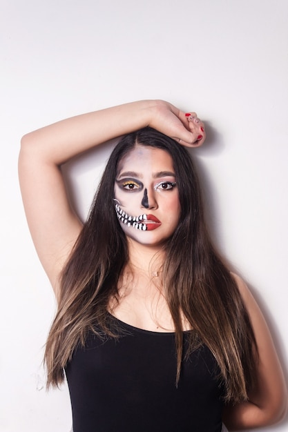 Portrait of a girl with Halloween skull makeup raising an arm above her head on white background.