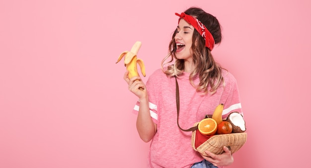 Portrait of a girl with healthy food, fruits, on a pink wall