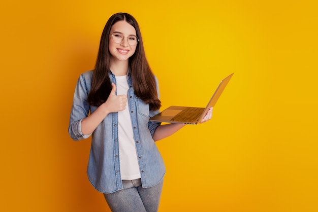 Portrait of girl with laptop posing hand chest on yellow background