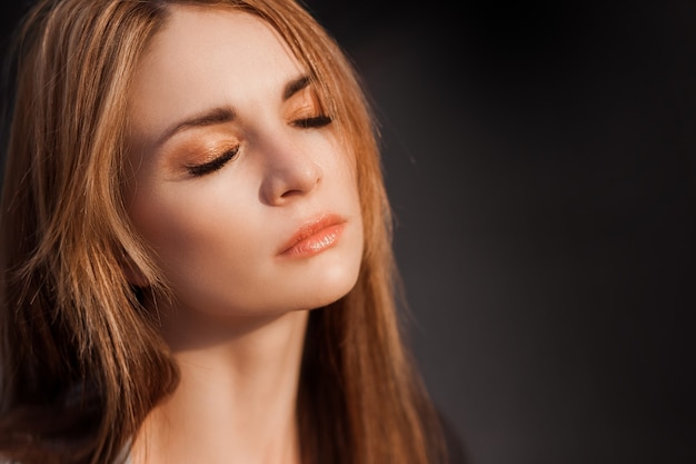 Portrait of a girl with long hair on a dark wall. Copy space