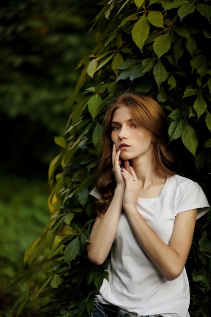 Portrait of a girl with long red hair in a green leaves