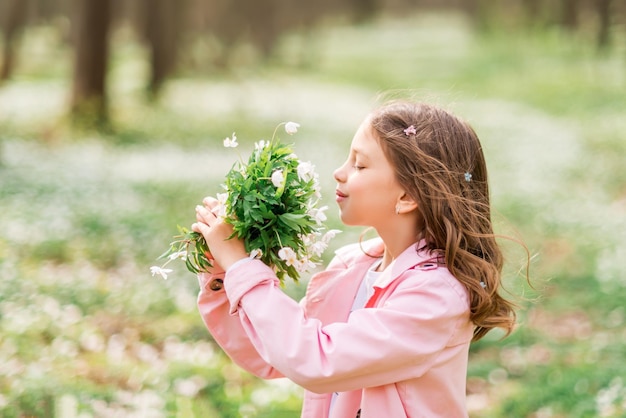 サクラソウの女の子の肖像春の森の子供が花の花束を嗅ぐ