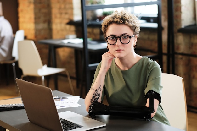 Portrait of girl with prosthesis arm working at office desk with laptop