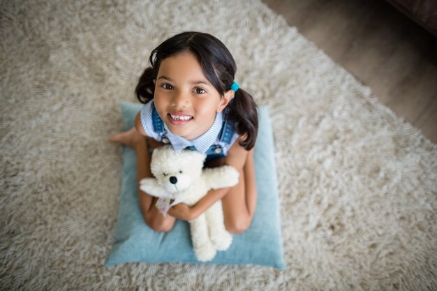 Portrait of girl with teddy bear sitting in living room