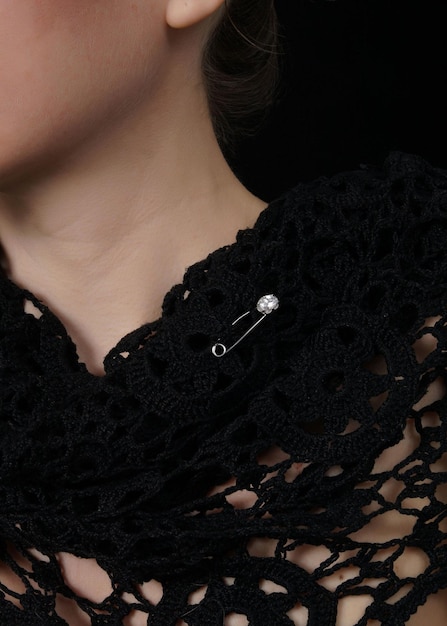 Photo portrait of girl with tied back dark hair wearing black shawl with perforated brooch the woman with black flicks is tilting her head posing against the black background closeup