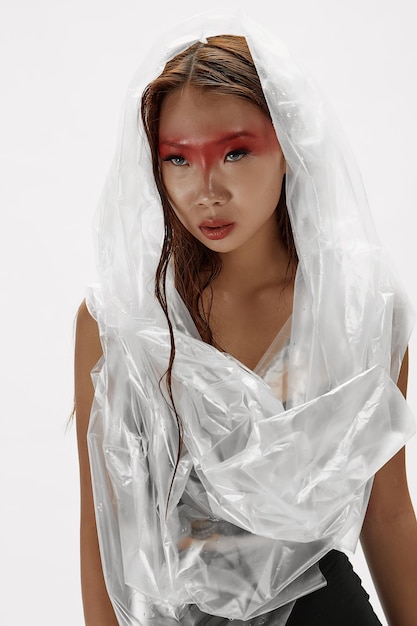 Portrait of a girl with wet hair and creative makeup in a cellophane hood