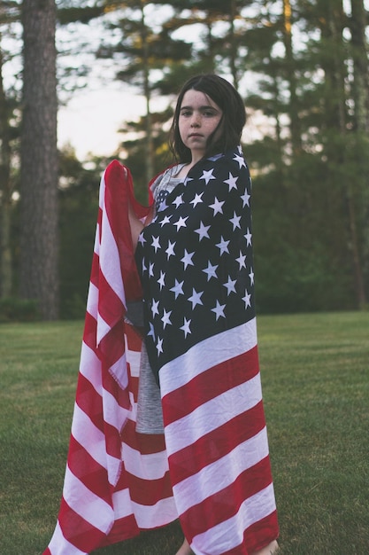 Photo portrait of girl wrapped in american flag while standing on field