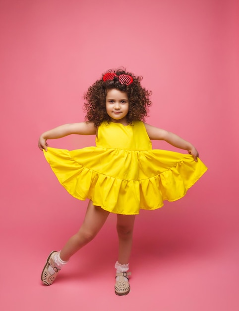 Portrait of a girl in a yellow dress cute attractive cute cheerful cheerful little girl isolated pink background