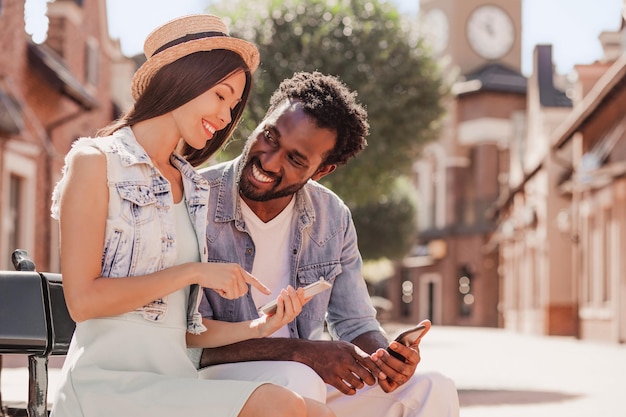 Portrait of girlfriend and boyfriend using smartphones sitting on the bench outdoors