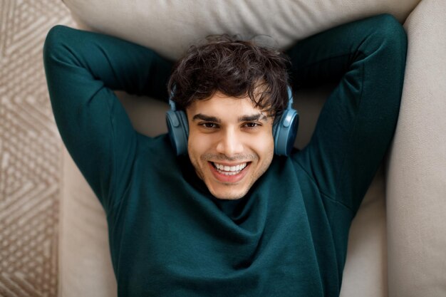 Portrait of glad young arab man with wireless earphones enjoys favorite music comfort and free time