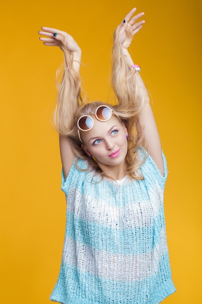 Portrait of glamorous beautiful blond woman in sunglasses and blue shirt on yellow background