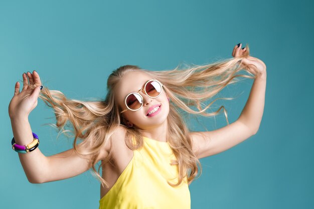 Portrait of glamorous beautiful blond woman in sunglasses and yellow shirt on blue background. Carefree summer.