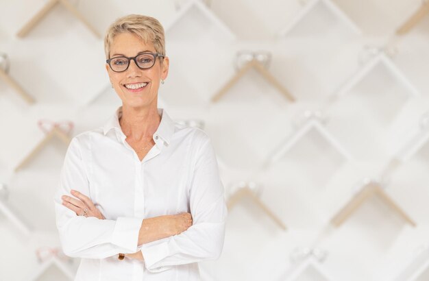 Portrait glasses and vision with a woman optometrist standing arms crossed alone in her optometry store Ophthalmology eyewear and frame with a mature female optician selling frame lenses