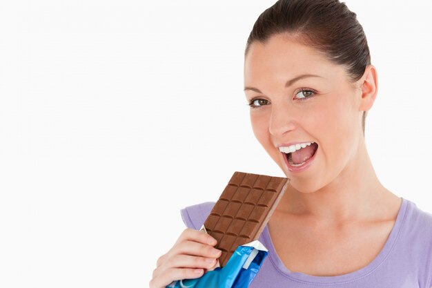 Portrait of a good looking woman eating a chocolate block while standing