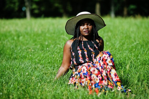 Portrait of gorgeous african american woman 20s in summer hat sitting at green grass in park