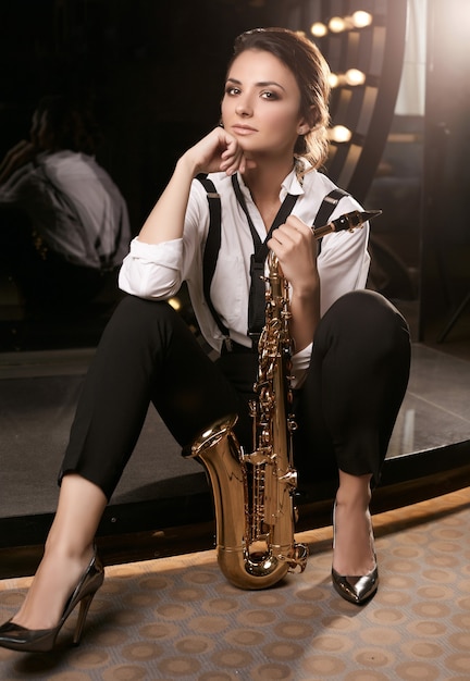 Portrait of gorgeous brunette model woman in fashionable formal suit with saxophone playing