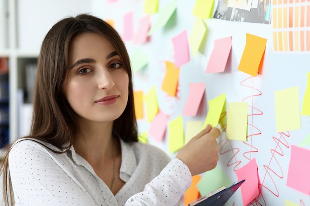 Portrait of gorgeous designer standing in modern office and holding yellow empty sticker.