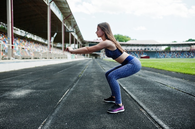 Portrait of a gorgeous girl doing squats in the stadium.