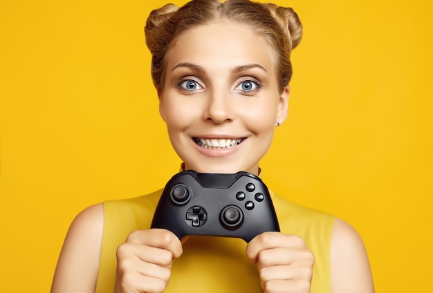 Portrait of gorgeous happy blonde gamer girl playing video games using joystick on yellow wall in studio