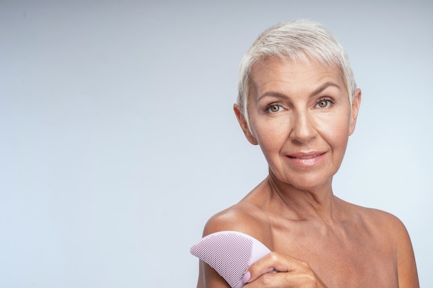 Portrait of a gorgeous mature woman hugging herself and holding face cleaner